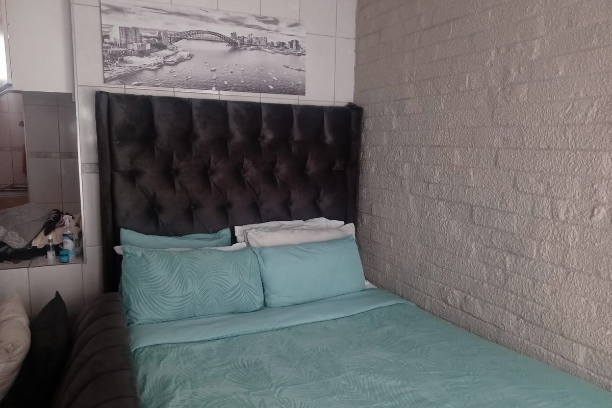 A bedroom featuring a textured brick feature wall and tiled wall section, providing a compact sleeping space.