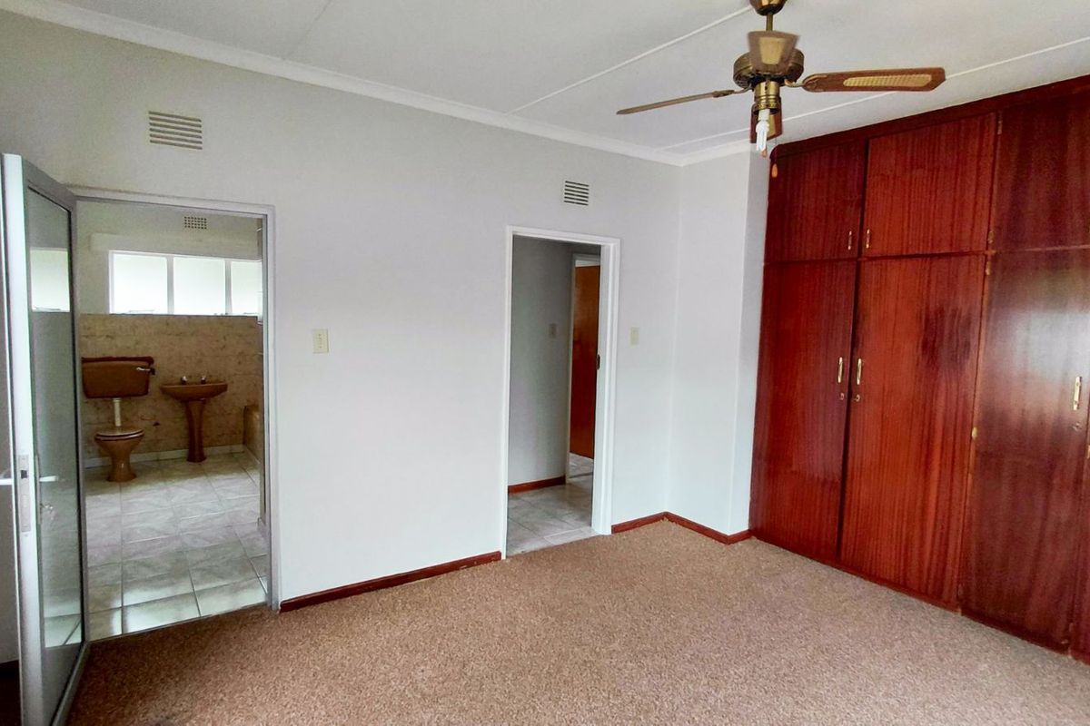 A bedroom featuring built-in wooden wardrobes, carpeted flooring, and a ceiling fan, with an adjoining bathroom visible through the doorway.