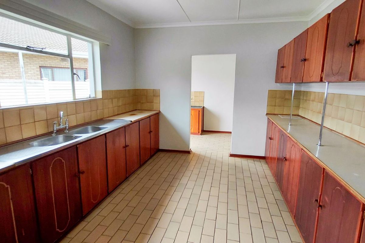 A functional kitchen featuring extensive wooden cabinetry, double stainless steel sink, and tiled splashbacks, offering a practical layout with potential for modernization.