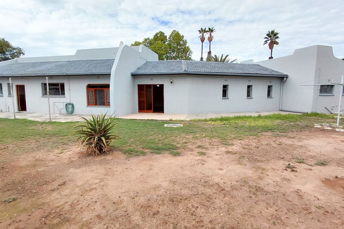 A view of the rear exterior of the house, featuring a paved patio area, tiled roof, and a large backyard with established trees.