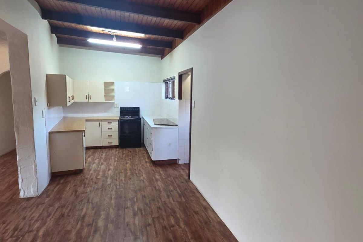 A functional kitchen area featuring wooden cabinetry, laminate countertops, a freestanding stove, and exposed timber ceiling beams, flowing into an adjacent living space.