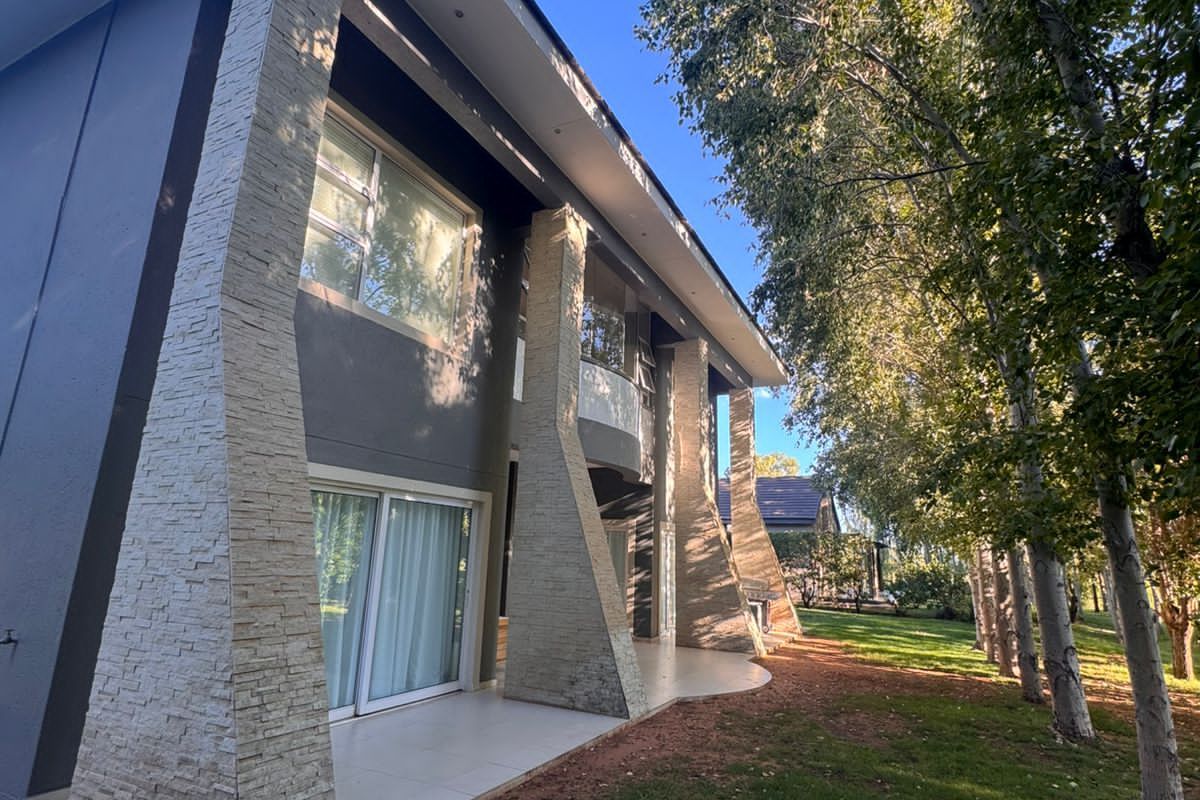 A view of the rear exterior facade featuring stone-clad structural pillars, tiled patio flooring, and large sliding glass doors overlooking the garden.