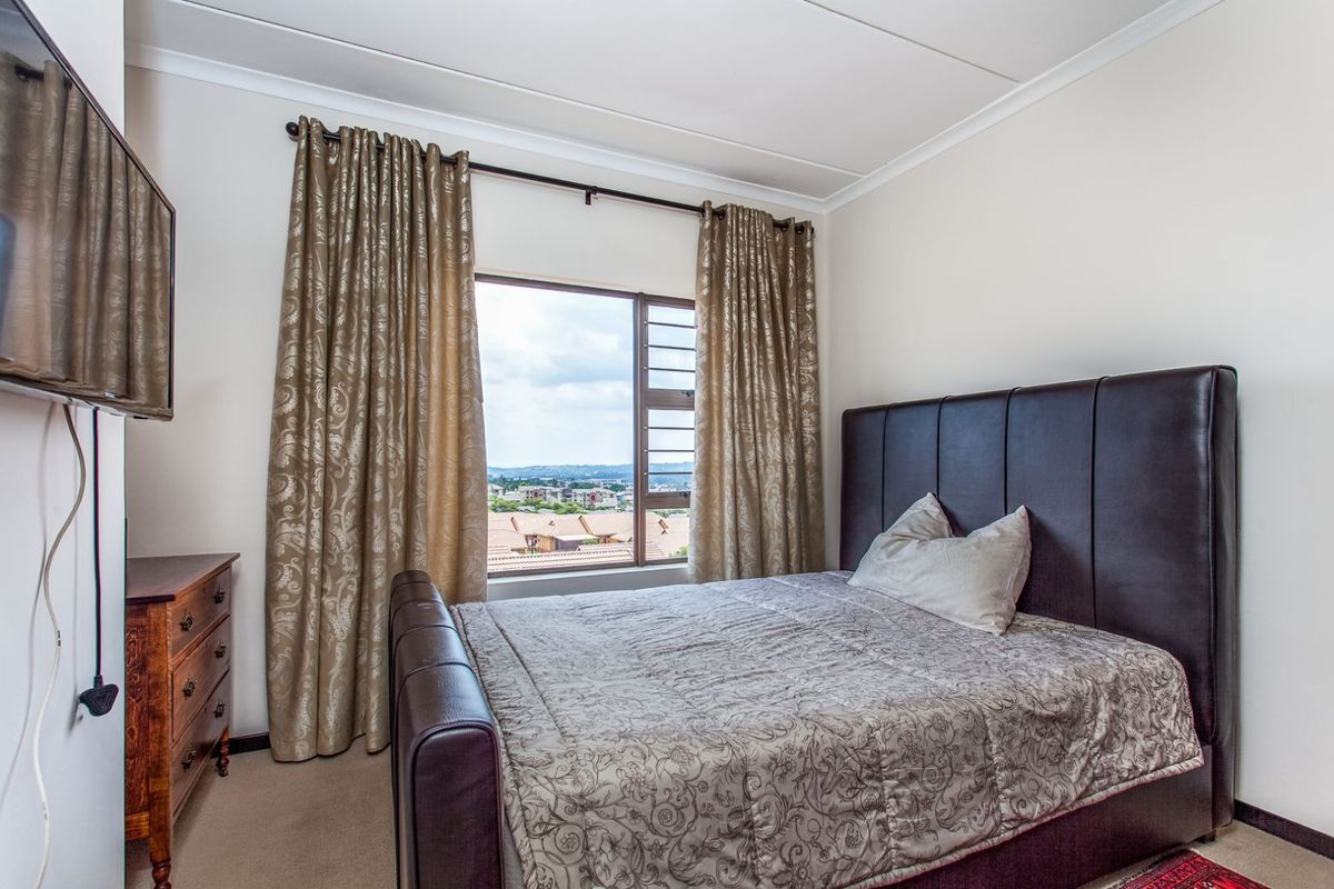 A well-lit bedroom featuring neutral walls, carpeted flooring, and a window offering an elevated view of the surrounding neighborhood.