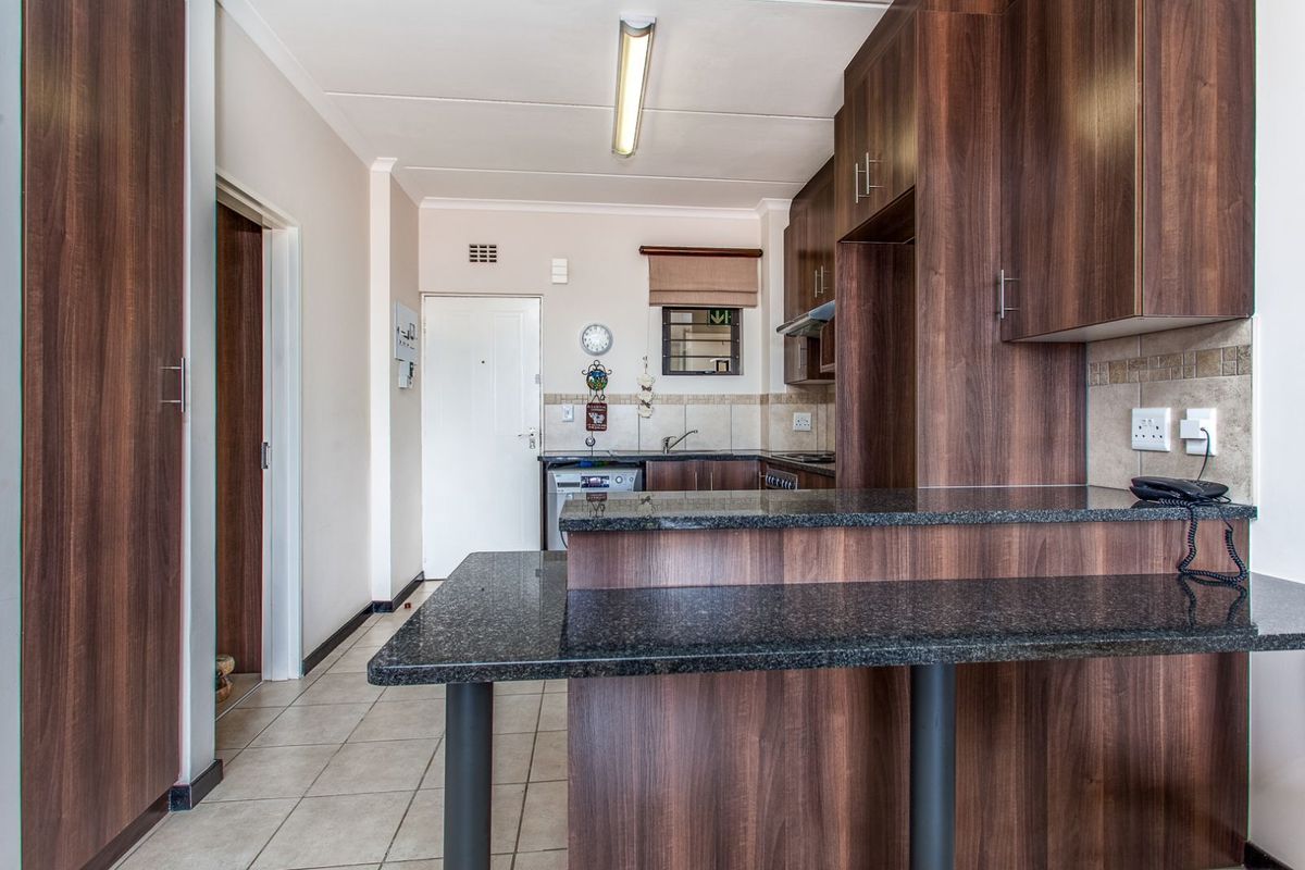 A functional kitchen featuring dark wood cabinetry, granite countertops, a breakfast bar, tiled flooring, and a built-in extractor fan.