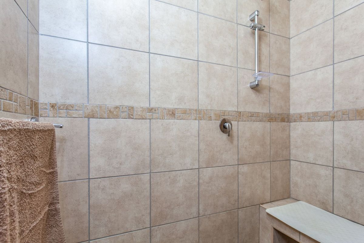 A tiled shower enclosure featuring a built-in bench, wall-mounted shower mixer, and adjustable shower head rail.