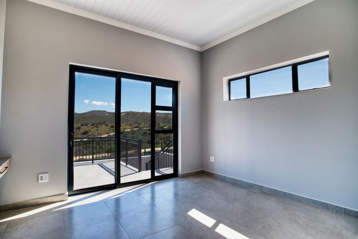 Bright, modern bedroom featuring large sliding glass doors leading to a balcony, tiled flooring, and neutral wall finishes with scenic landscape views.