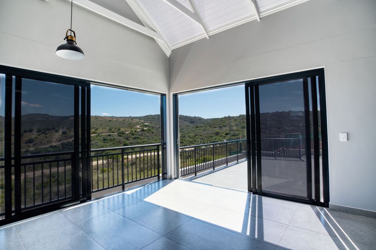 A bright, modern living space featuring high vaulted ceilings, tiled flooring, and large sliding glass doors opening onto a balcony with scenic landscape views.