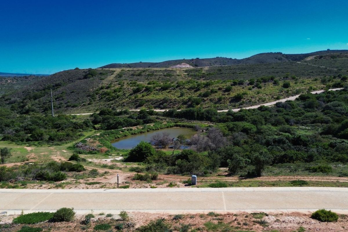 An aerial view of the property landscape featuring natural vegetation, a small pond, and surrounding hilly terrain.
