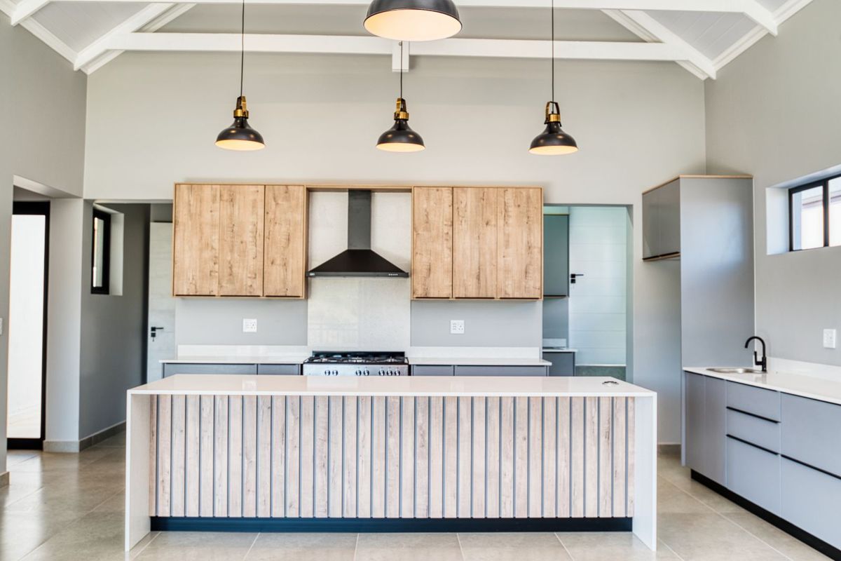 Modern kitchen featuring a central island with wood-panel detailing, stone countertops, built-in gas hob, extractor fan, and sleek grey cabinetry under a vaulted ceiling.