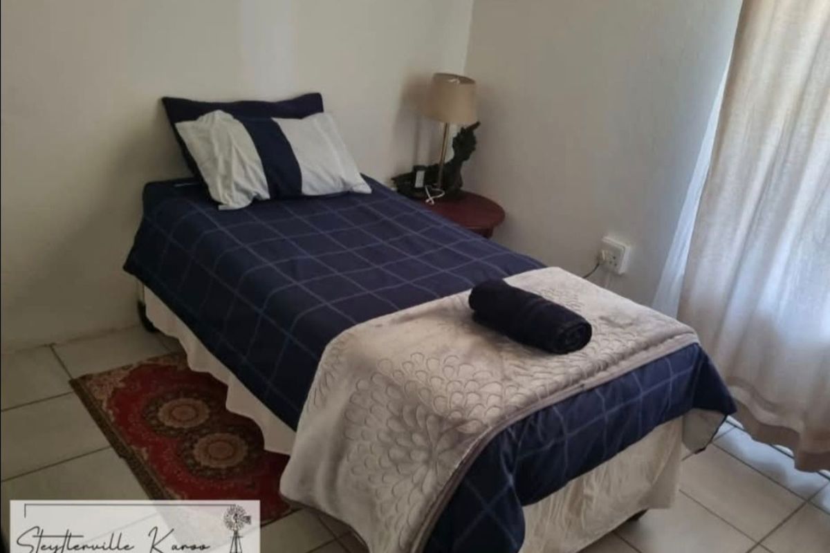 A simple bedroom featuring tiled flooring and a window with curtains.
