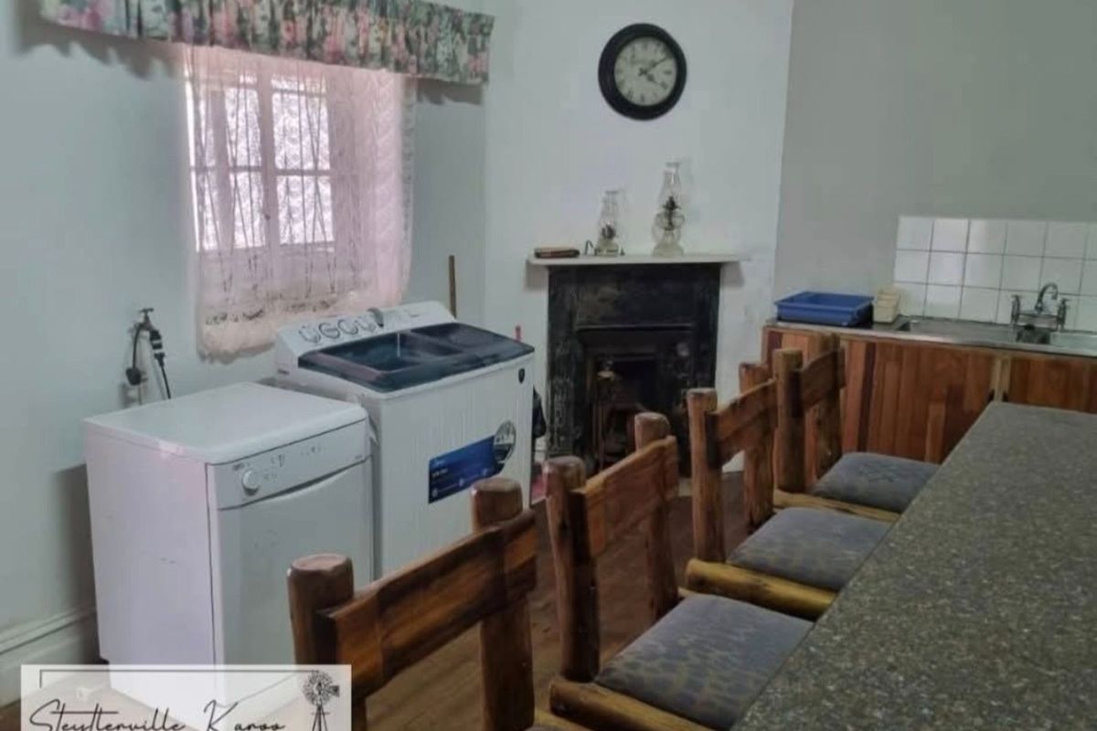 A rustic kitchen area featuring wooden cabinetry, a built-in sink, and a traditional fireplace, with integrated laundry appliance connections.