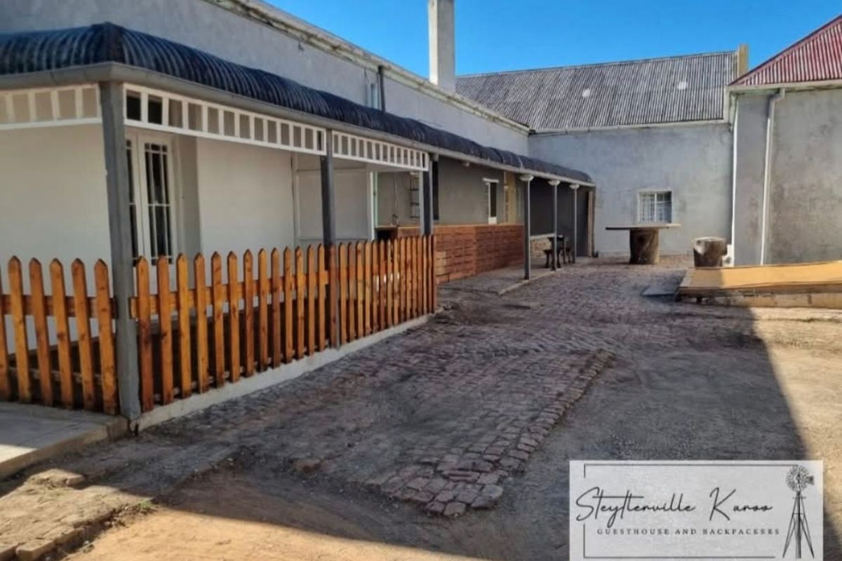 A rear exterior view of the property featuring a covered patio area, brick paving, and a wooden fence enclosure.