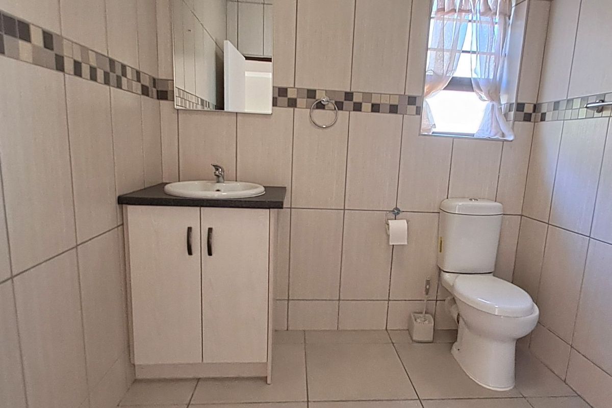 A functional bathroom featuring floor-to-ceiling wall tiles, a vanity cabinet with a basin, and a standard toilet.