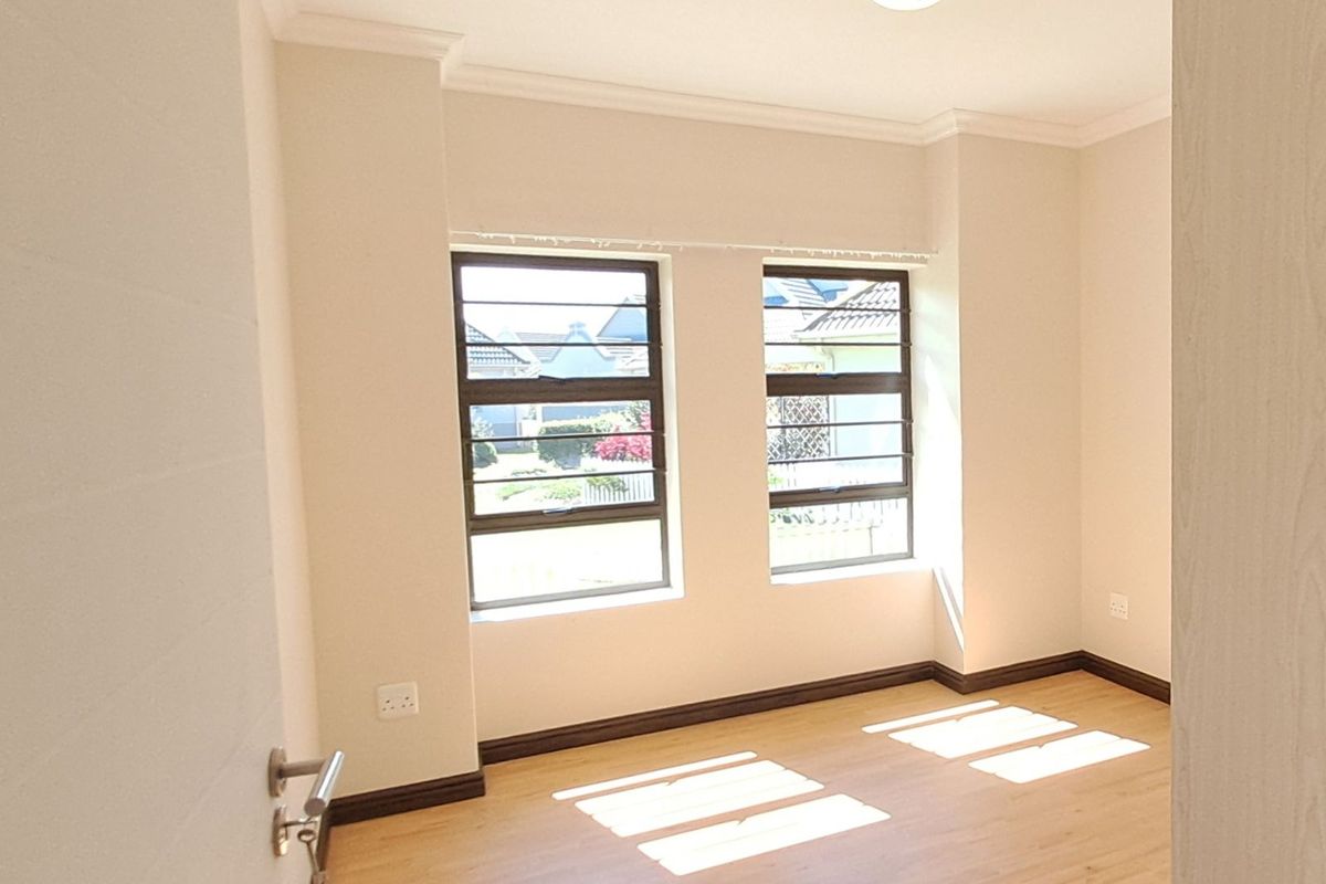 A bright, empty bedroom featuring light-toned laminate flooring, neutral walls, and two windows with security bars.
