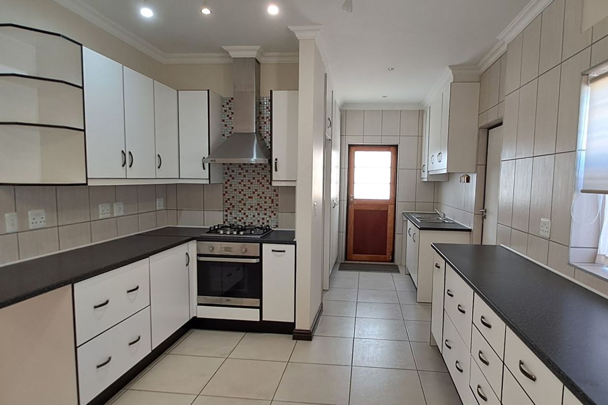 A functional kitchen featuring white cabinetry, dark countertops, a built-in oven with extractor fan, and tiled flooring throughout.