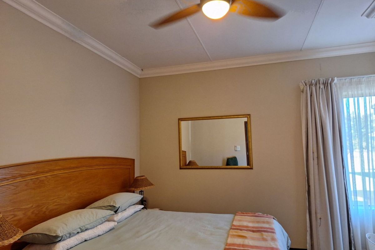 A bedroom featuring a ceiling fan, crown molding, and a window with curtains, providing a functional and comfortable living space.