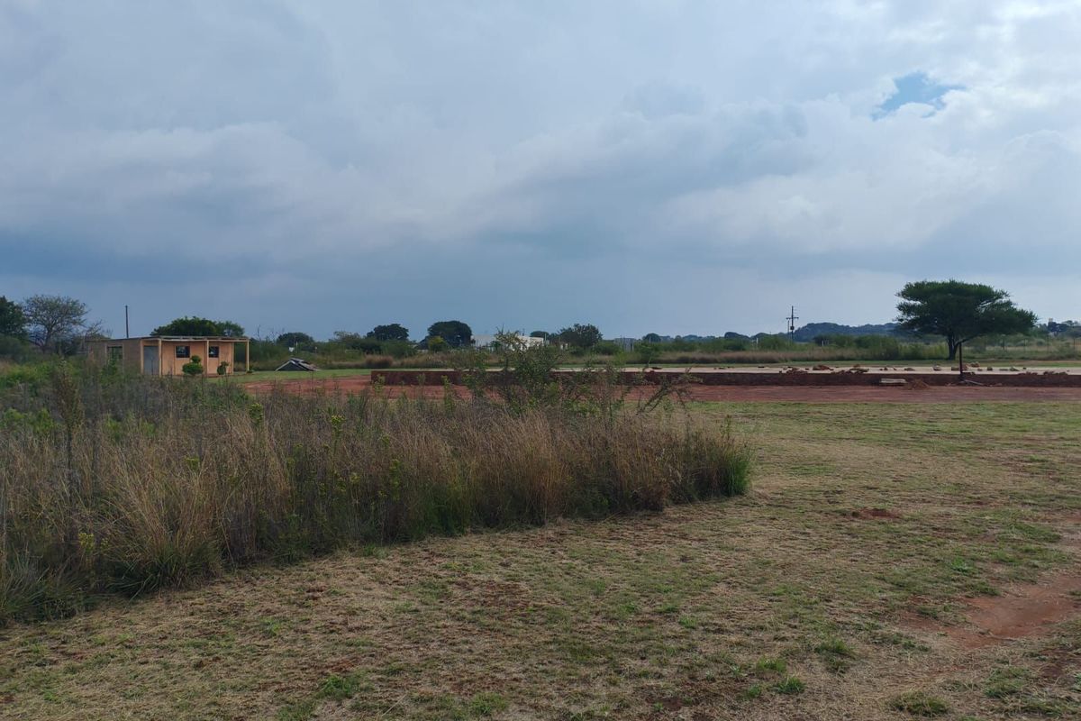 A view of a vacant residential plot featuring natural vegetation, a small existing structure, and a cleared area for potential development.