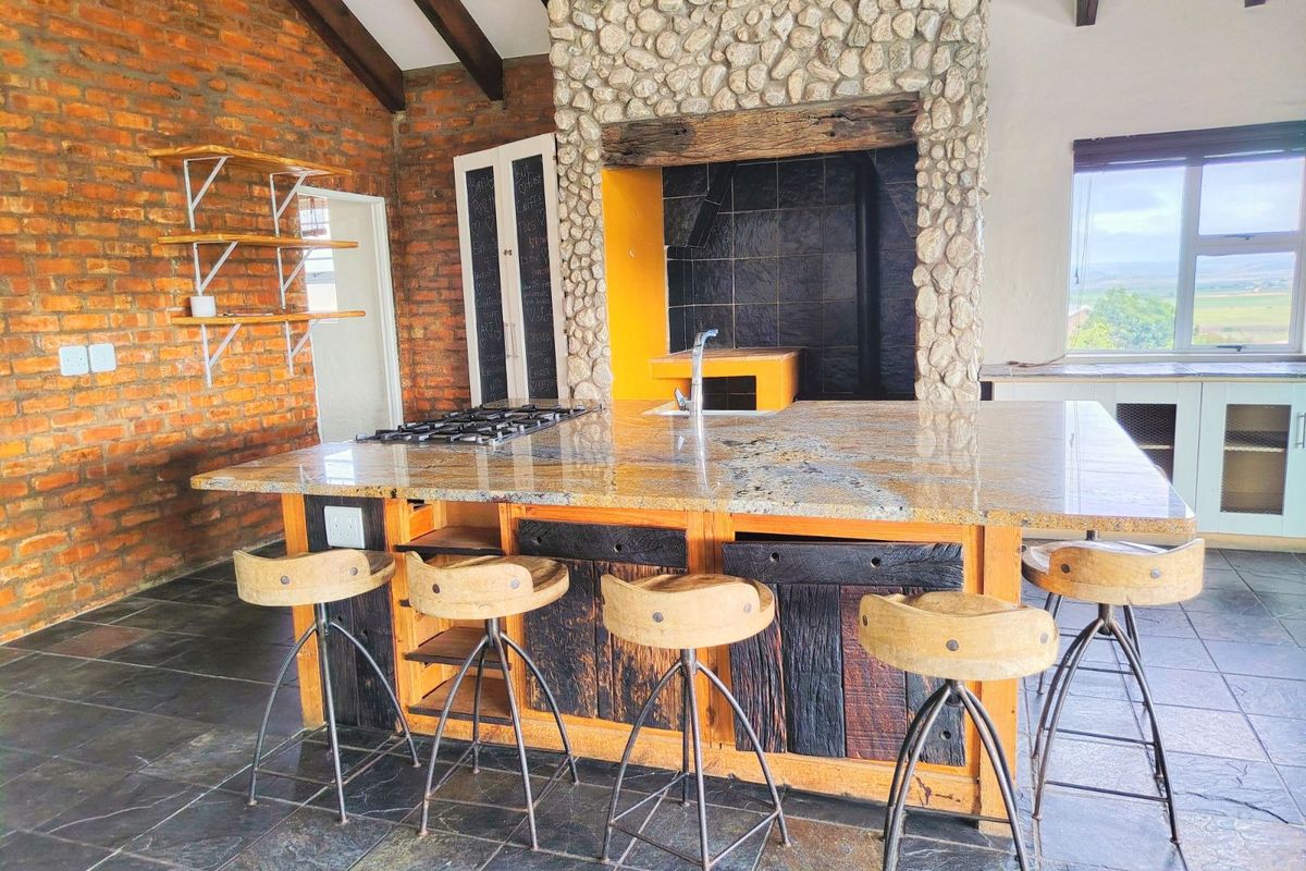 Rustic kitchen featuring a large stone-clad fireplace, granite island countertop with integrated gas hob and sink, exposed brick walls, and slate flooring.
