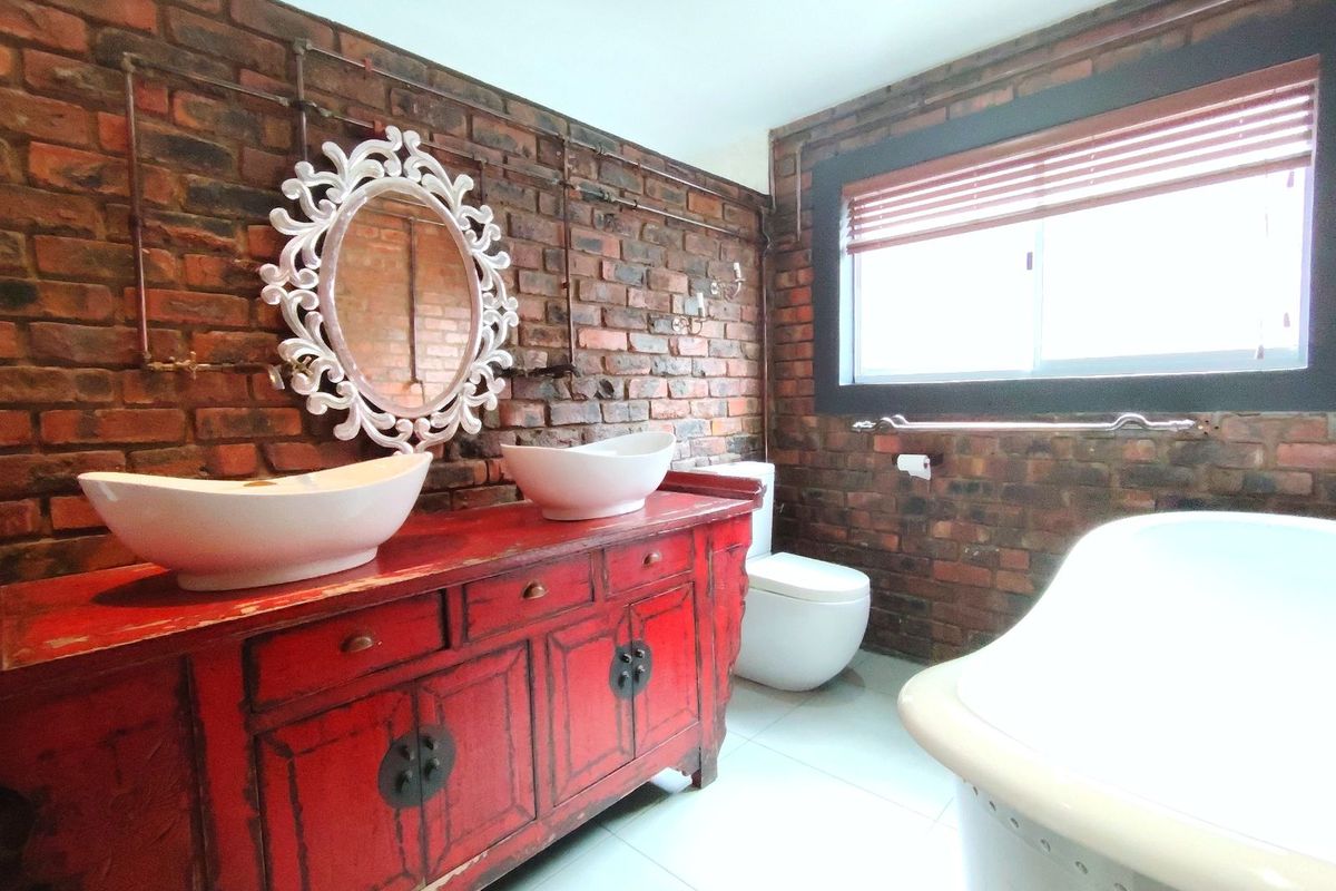 A characterful bathroom featuring exposed brick walls, a double vanity with vessel sinks, a freestanding bathtub, and a modern toilet.