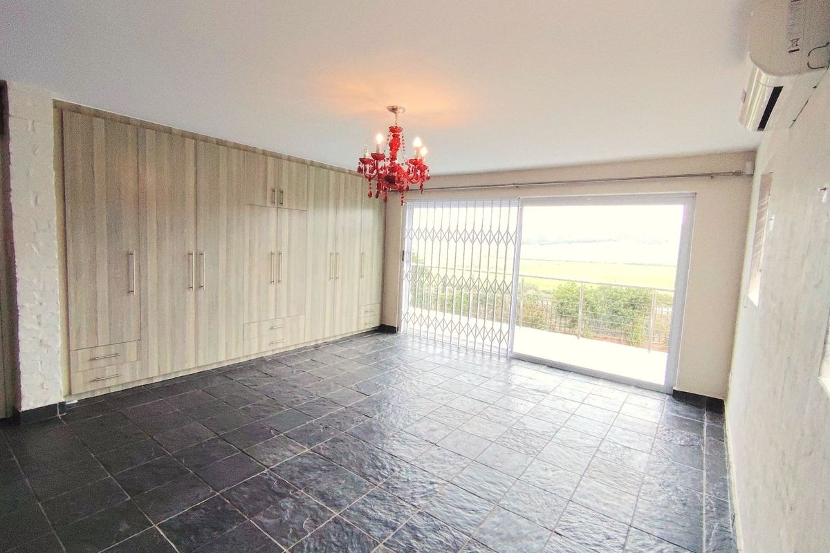 Spacious bedroom featuring built-in wooden cabinetry, dark tiled flooring, and sliding glass doors opening to a balcony with scenic views.