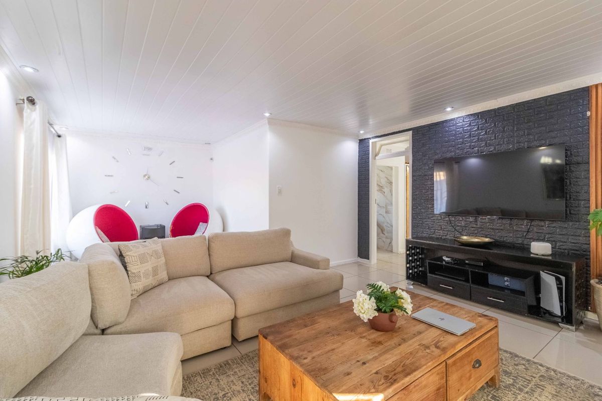 A modern living room featuring a dark brick-style feature wall, recessed downlighting, and tiled flooring throughout.
