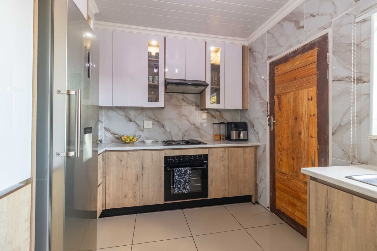 Modern kitchen featuring wood-look lower cabinetry, white upper cabinets, marble-effect wall tiles, built-in oven, and hob with extractor fan.