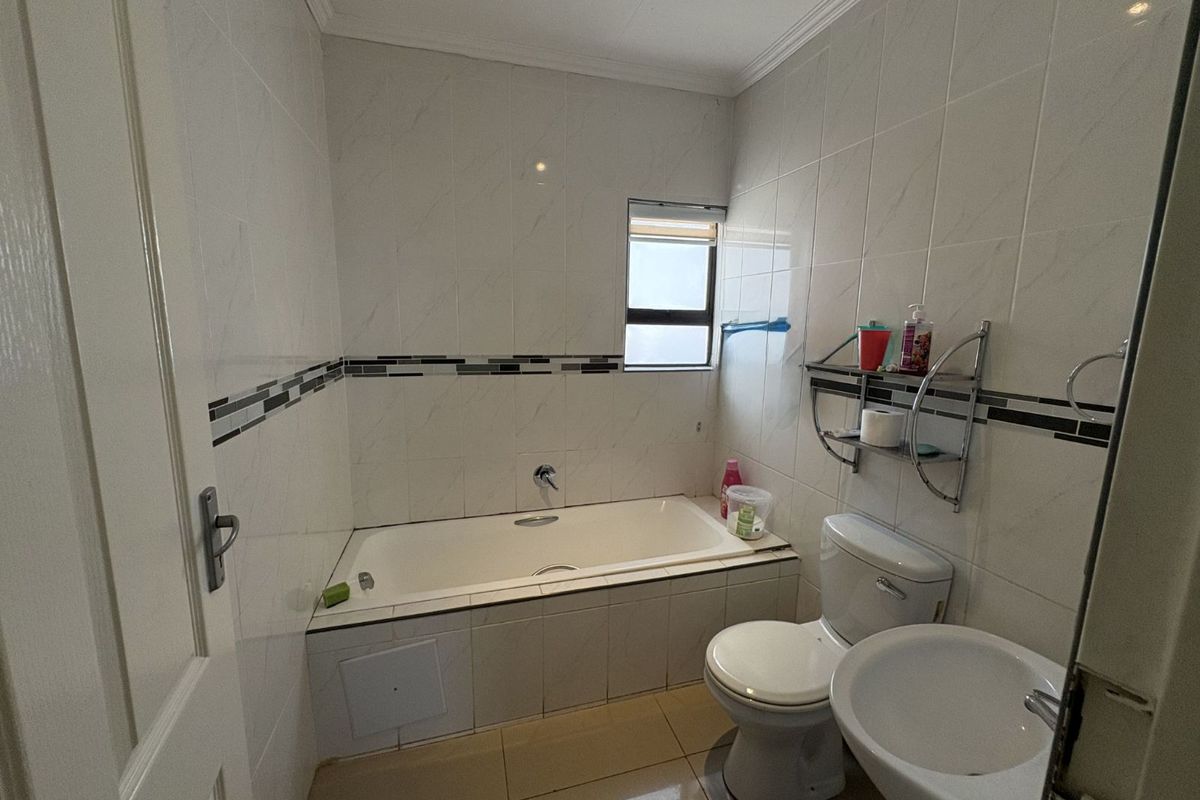 A functional bathroom featuring a built-in bathtub, pedestal basin, and toilet, finished with neutral wall tiles and a decorative border.