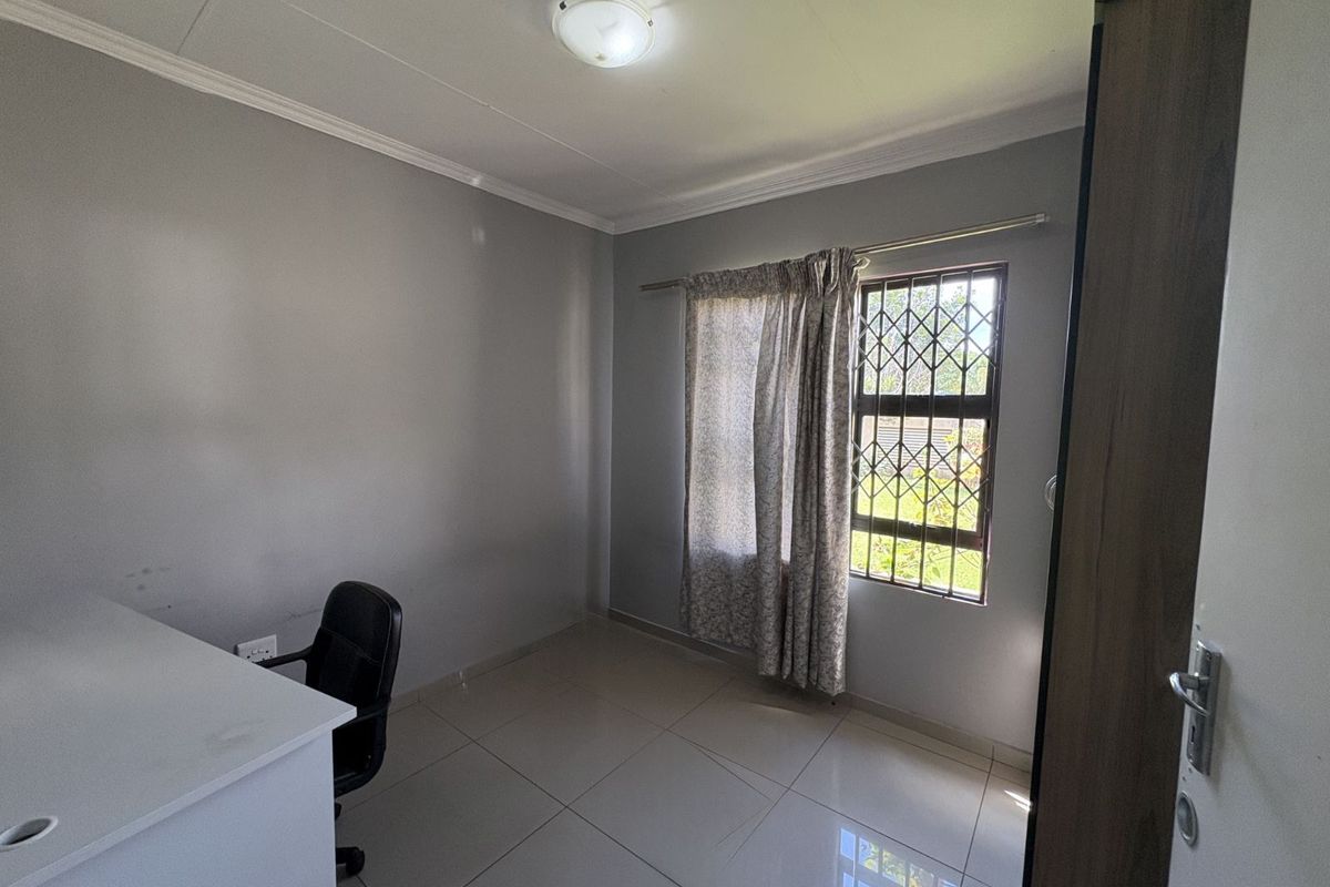 A functional bedroom featuring neutral grey walls, tiled flooring, and a window fitted with security bars.