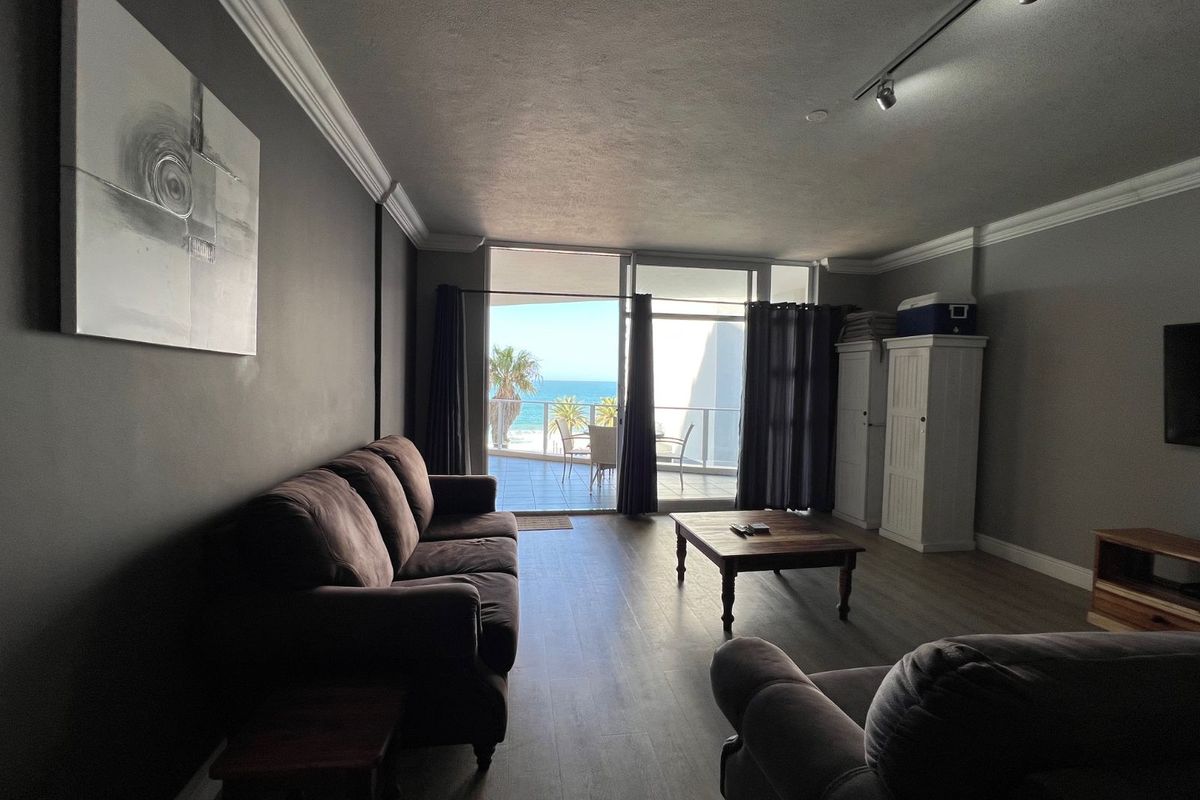 Spacious living room featuring wood-look flooring, crown molding, and large sliding glass doors opening onto a balcony with ocean views.