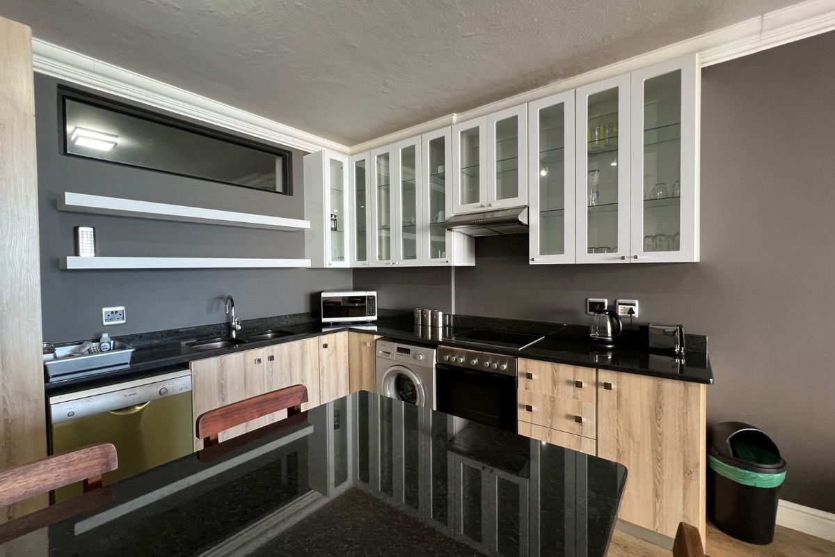 Modern kitchen featuring light wood cabinetry, black granite countertops, integrated appliances, and glass-fronted upper cabinets with a clean, contemporary finish.
