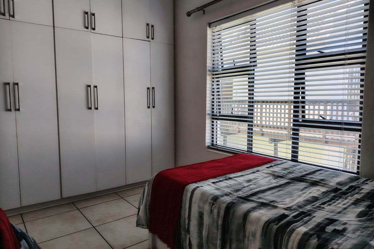 A well-lit bedroom featuring floor-to-ceiling built-in cupboards and large windows with fitted blinds, offering a clean and functional living space.