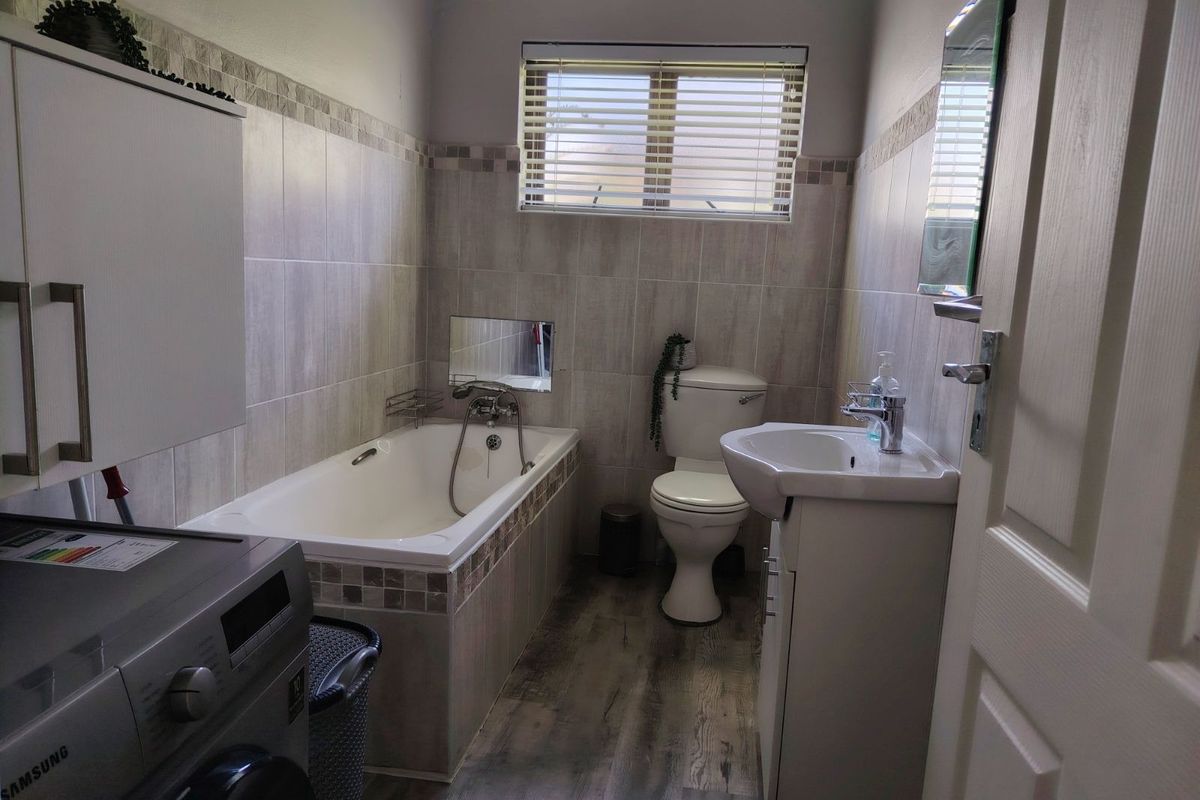 A functional bathroom featuring a built-in bathtub, a pedestal vanity with a basin, a toilet, and tiled wall finishes with a neutral aesthetic.