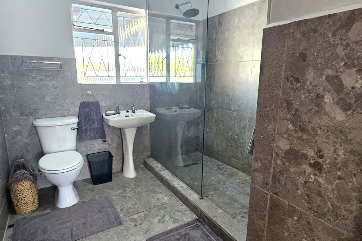 A modern bathroom featuring grey stone-look wall and floor tiles, a pedestal basin, a toilet, and a walk-in shower with a glass screen.