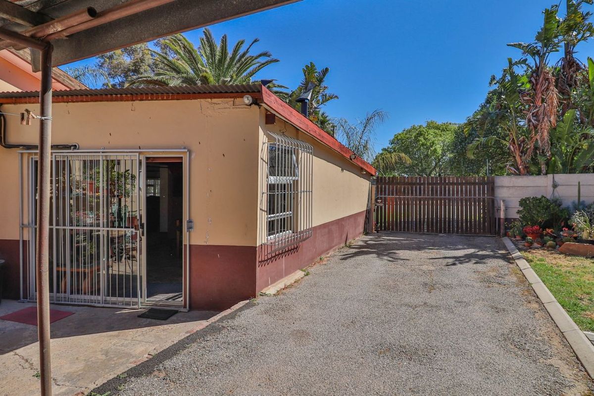 Rear exterior view of the property featuring a gravel driveway, security gate, and access to the interior through a sliding door with security bars.
