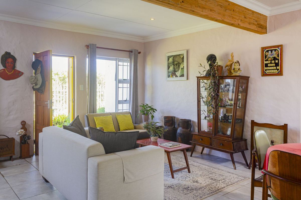A bright living area featuring tiled flooring, exposed timber ceiling beams, and direct access to the outdoor space through a wooden door.