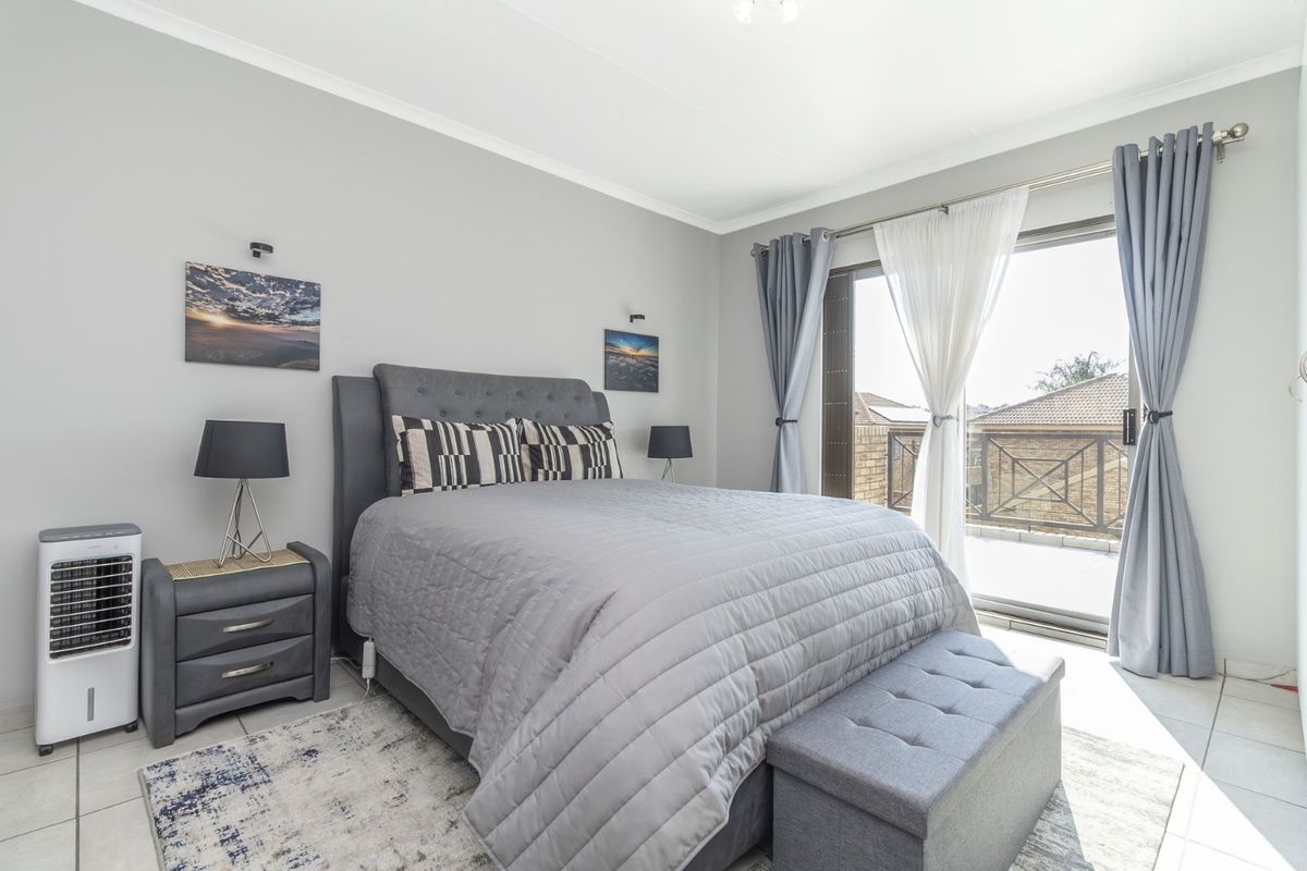 A well-maintained bedroom featuring neutral wall finishes, tiled flooring, and large sliding glass doors providing access to an outdoor balcony area.