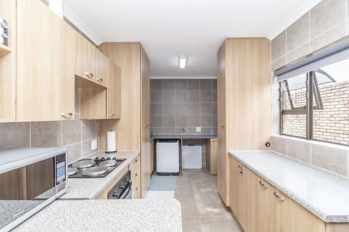 A functional kitchen and laundry area featuring light wood cabinetry, granite-look countertops, tiled splashbacks, and a built-in electric hob and oven.