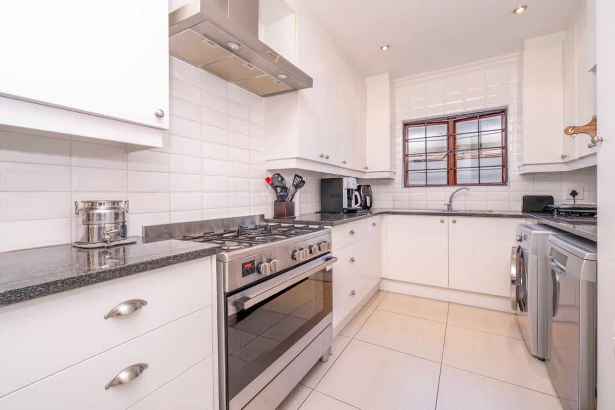 A well-maintained kitchen featuring white cabinetry, granite countertops, a stainless steel gas stove with extractor fan, and tiled flooring.