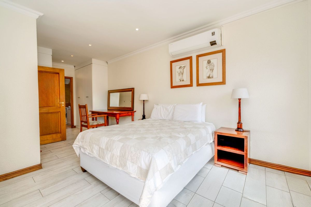 A well-maintained bedroom featuring tiled flooring, built-in cupboards, and a wall-mounted air conditioning unit.