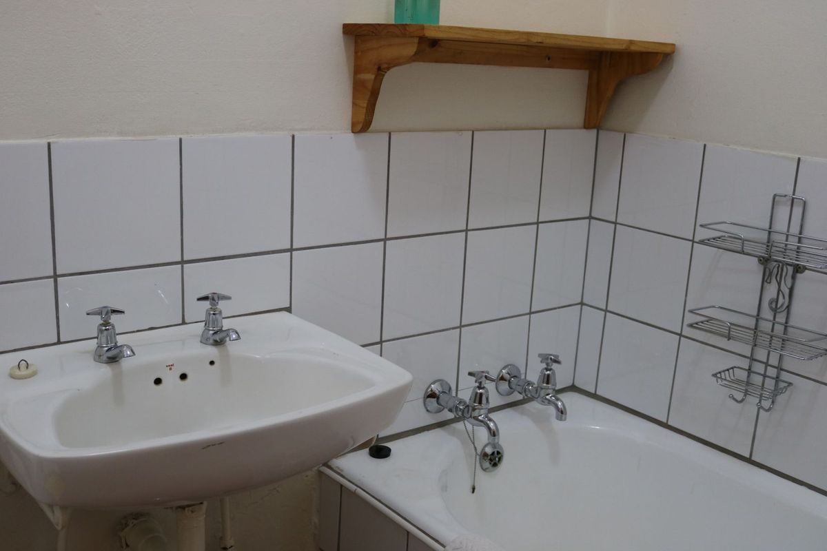 A functional bathroom featuring a white pedestal basin and a built-in bathtub with chrome tapware and tiled splashbacks.