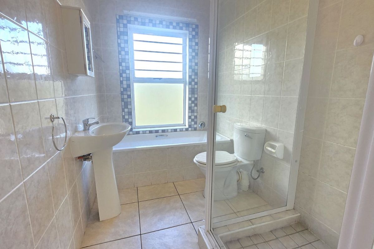 A functional bathroom featuring a pedestal basin, a built-in bathtub with tiled surround, and a separate glass-enclosed shower area.
