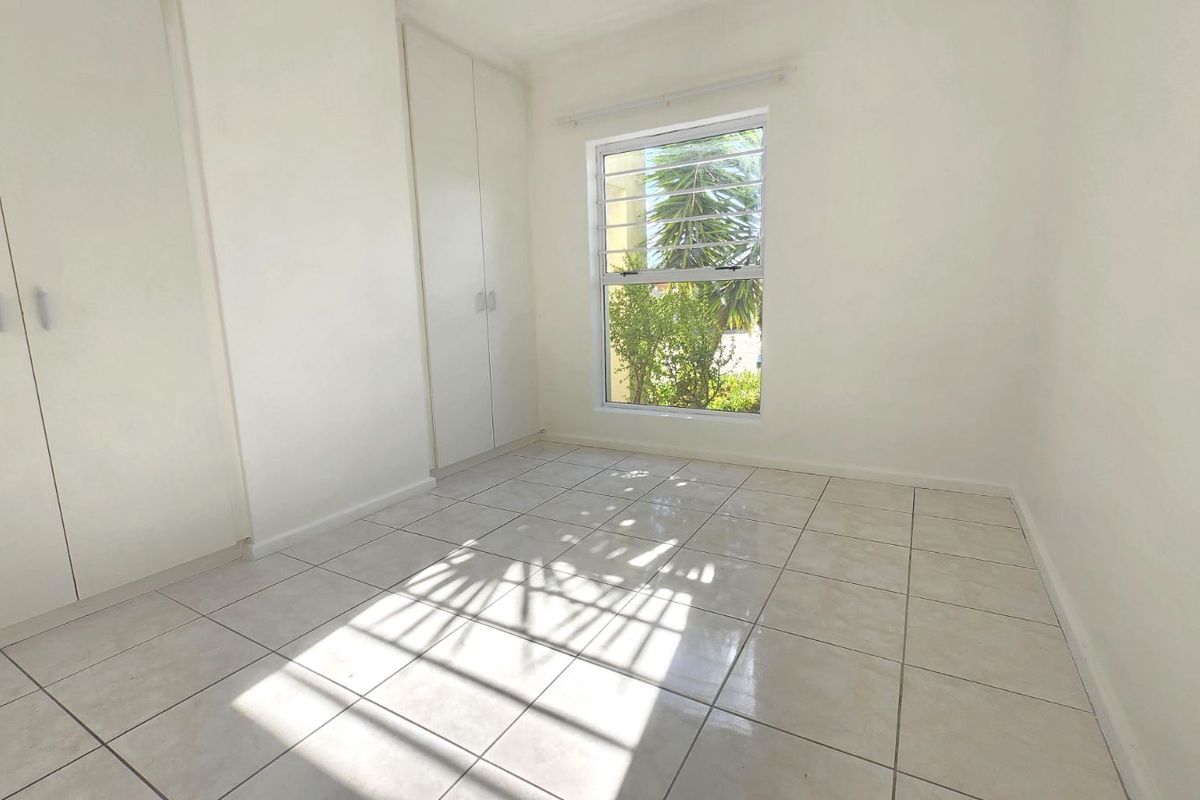 A bright, empty bedroom featuring neutral floor tiles and built-in cupboards, offering a clean and versatile space ready for personalization.