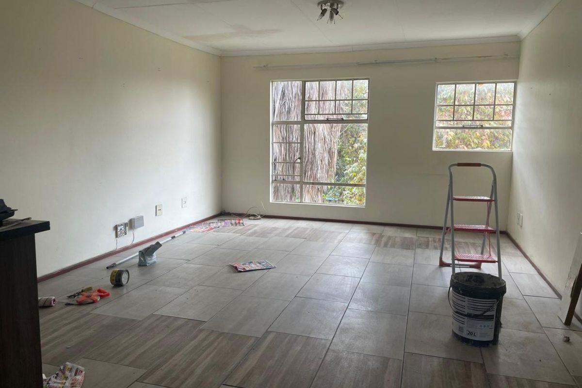 An empty living area featuring tiled flooring, large windows, and neutral walls, currently undergoing minor renovations and maintenance.