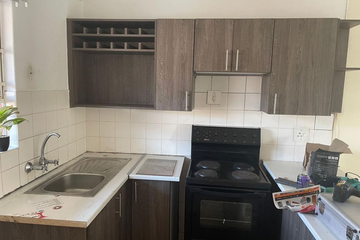 A compact kitchen featuring wood-grain cabinetry, a stainless steel sink, and a freestanding electric stove with tiled splashbacks.