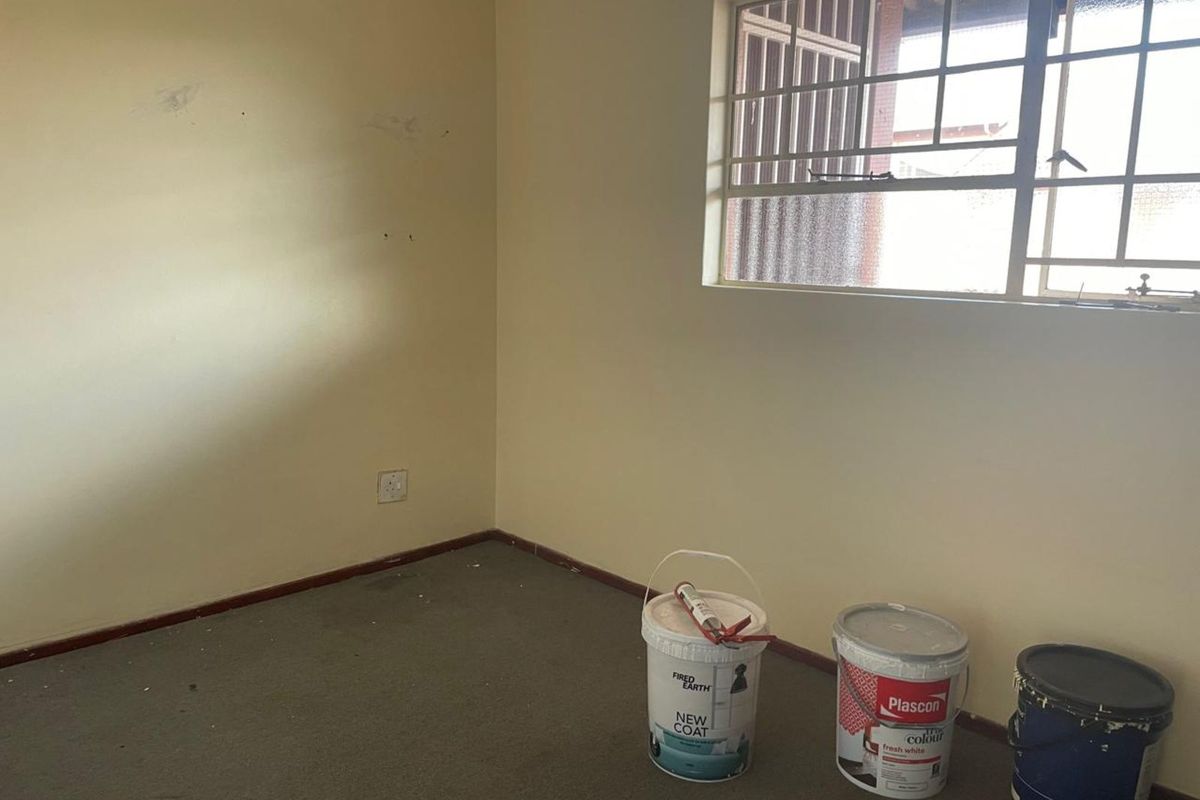A vacant bedroom featuring neutral walls, carpeted flooring, and a window with security bars, currently undergoing minor maintenance.