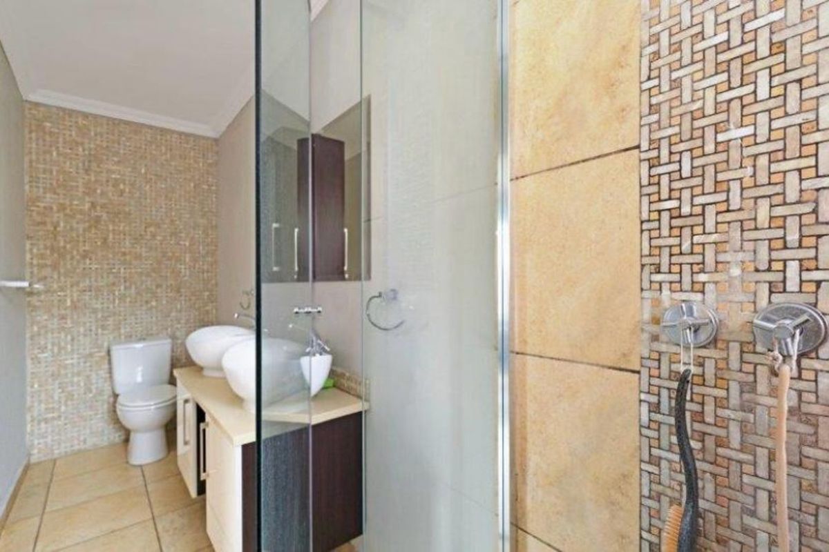 A modern bathroom featuring a glass-enclosed shower, dual vessel sinks on a vanity, and decorative mosaic tile accents.