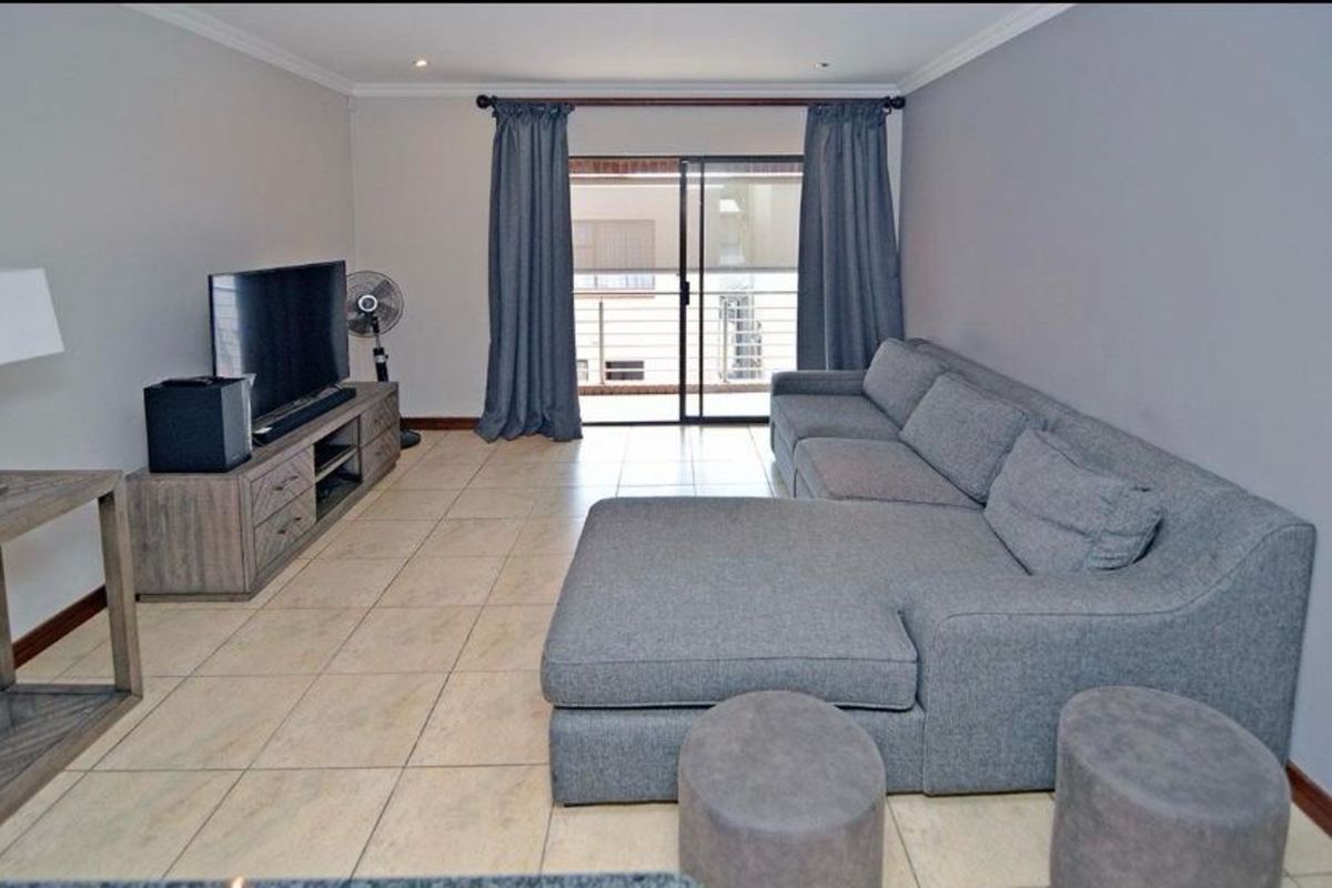 A spacious living room featuring neutral floor tiles, recessed ceiling lighting, and sliding glass doors that open onto a private balcony.
