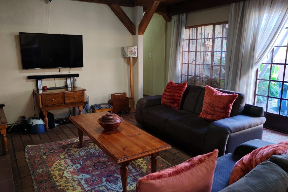 A cozy living room featuring exposed timber ceiling beams, terracotta tile flooring, and large glass doors providing access to the outdoor area.