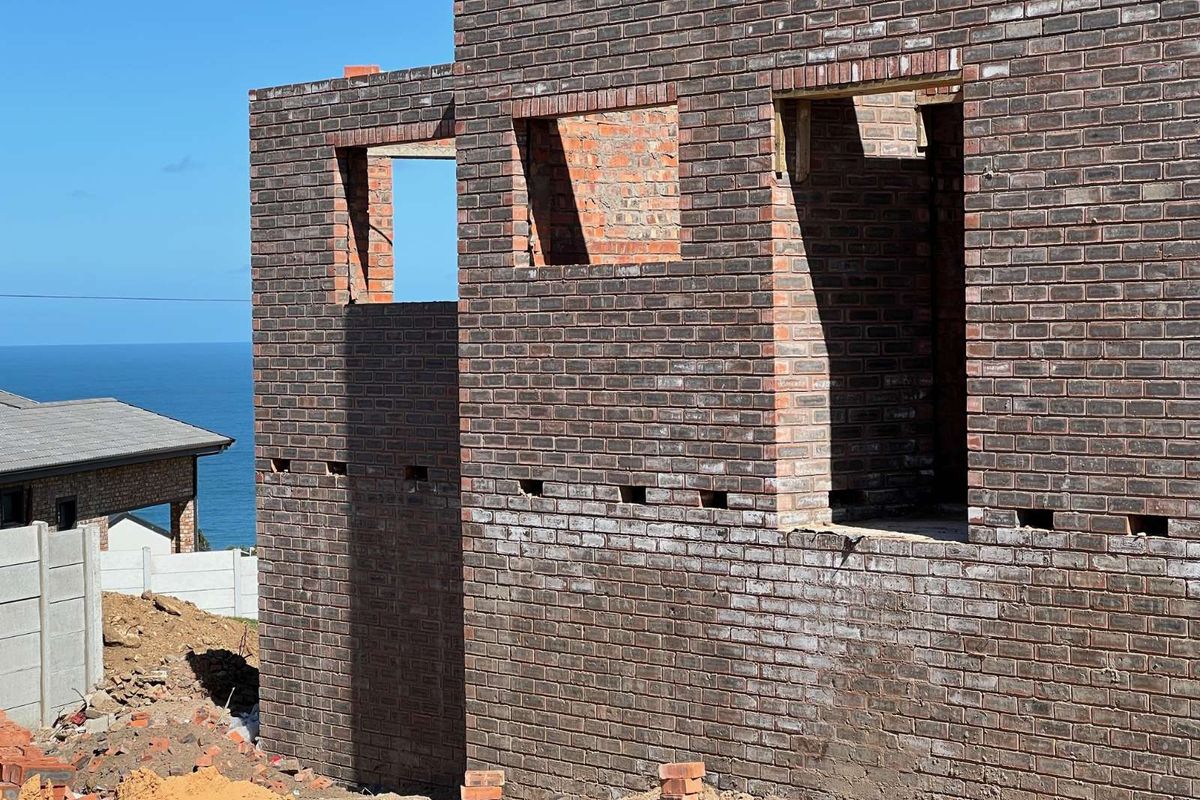 A view of a property under construction, featuring exposed brickwork and open window apertures with a coastal backdrop.