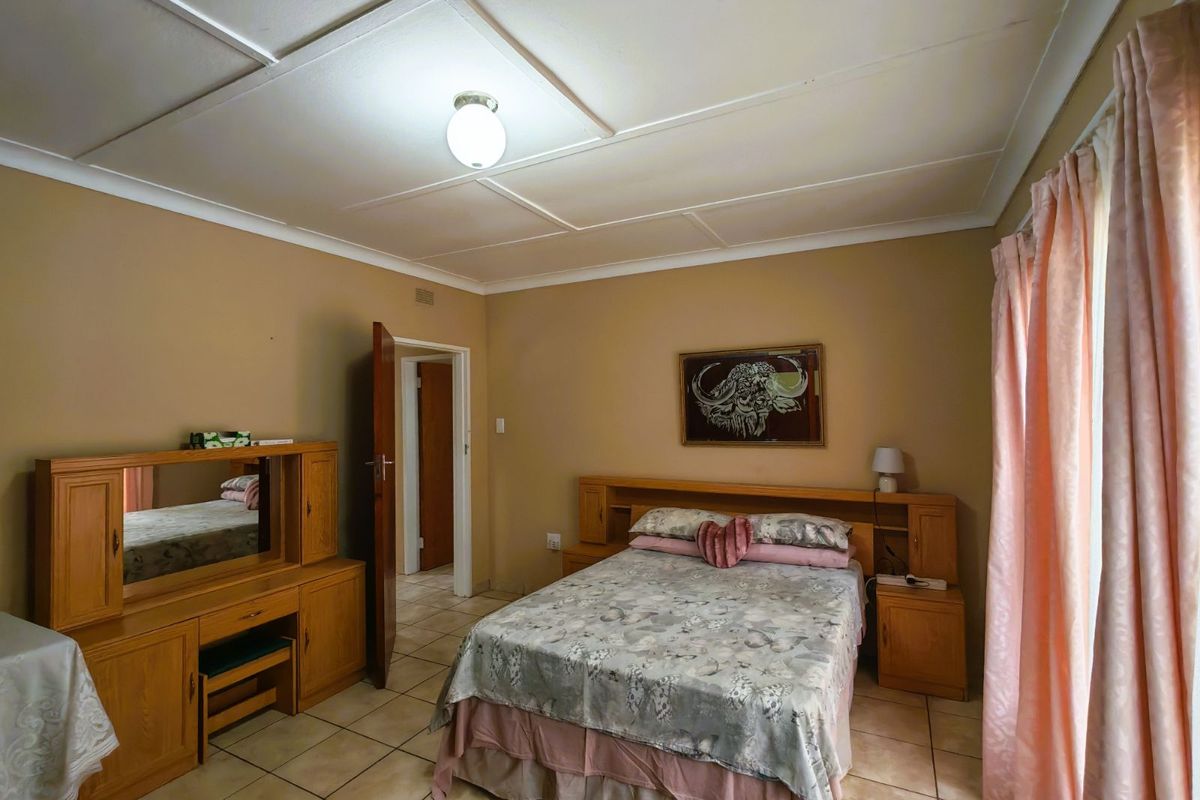 A bedroom featuring tiled flooring, built-in wooden headboard cabinetry, and a vanity unit, providing a functional and traditional living space.